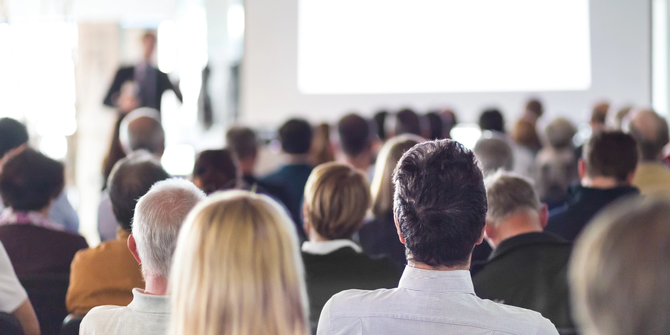 Une conférence remplie de monde et un conférencier présentant.