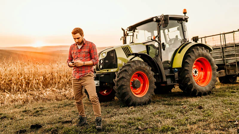 Man using cellphone in front of tractor at a wheatfield