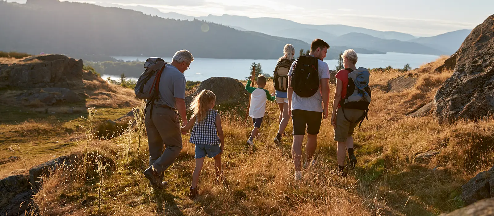 Rear view of multi generational family walking on top of a hill hiking through countryside