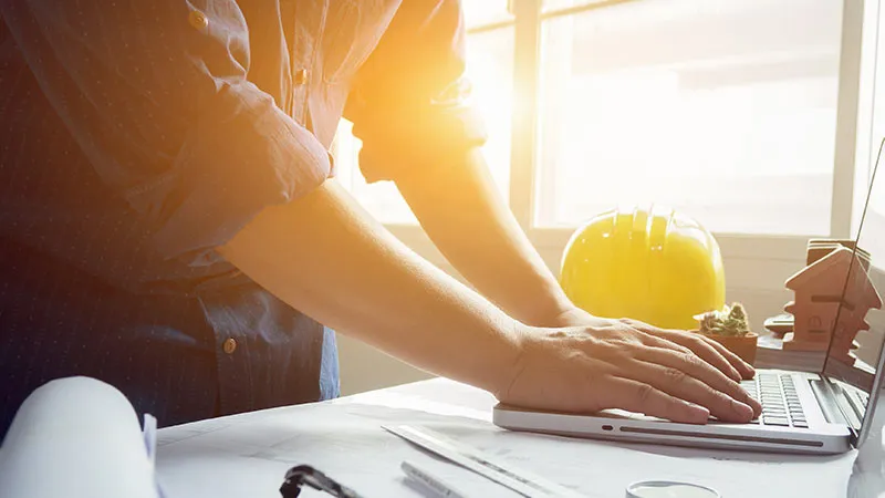 Person working on a laptop with a hard hat in the background