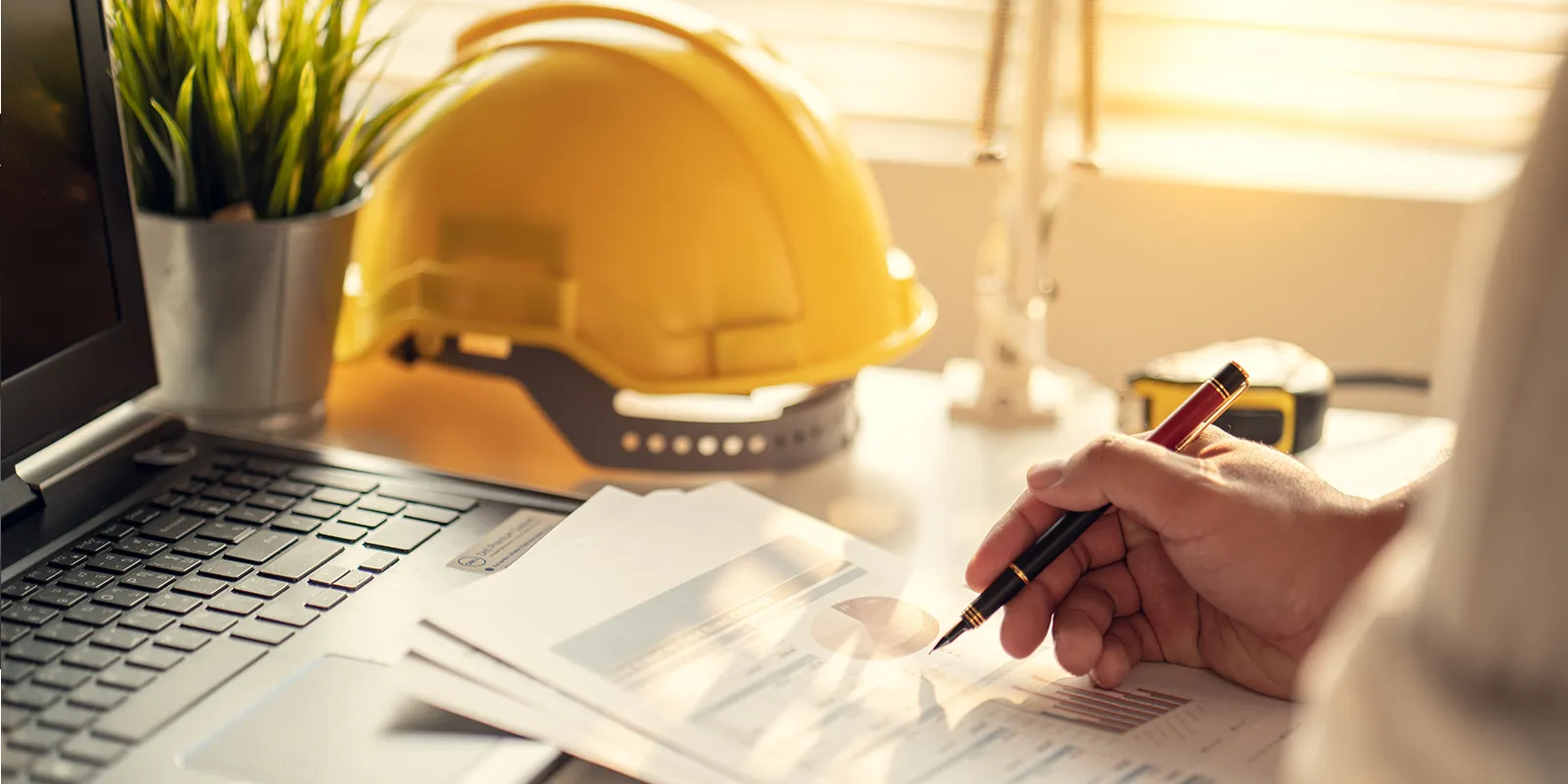 Construction leader writing in an office with a laptop at a desk.