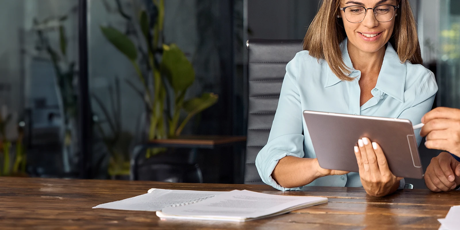 Femme professionnelle regardant une tablette, assise à une table.