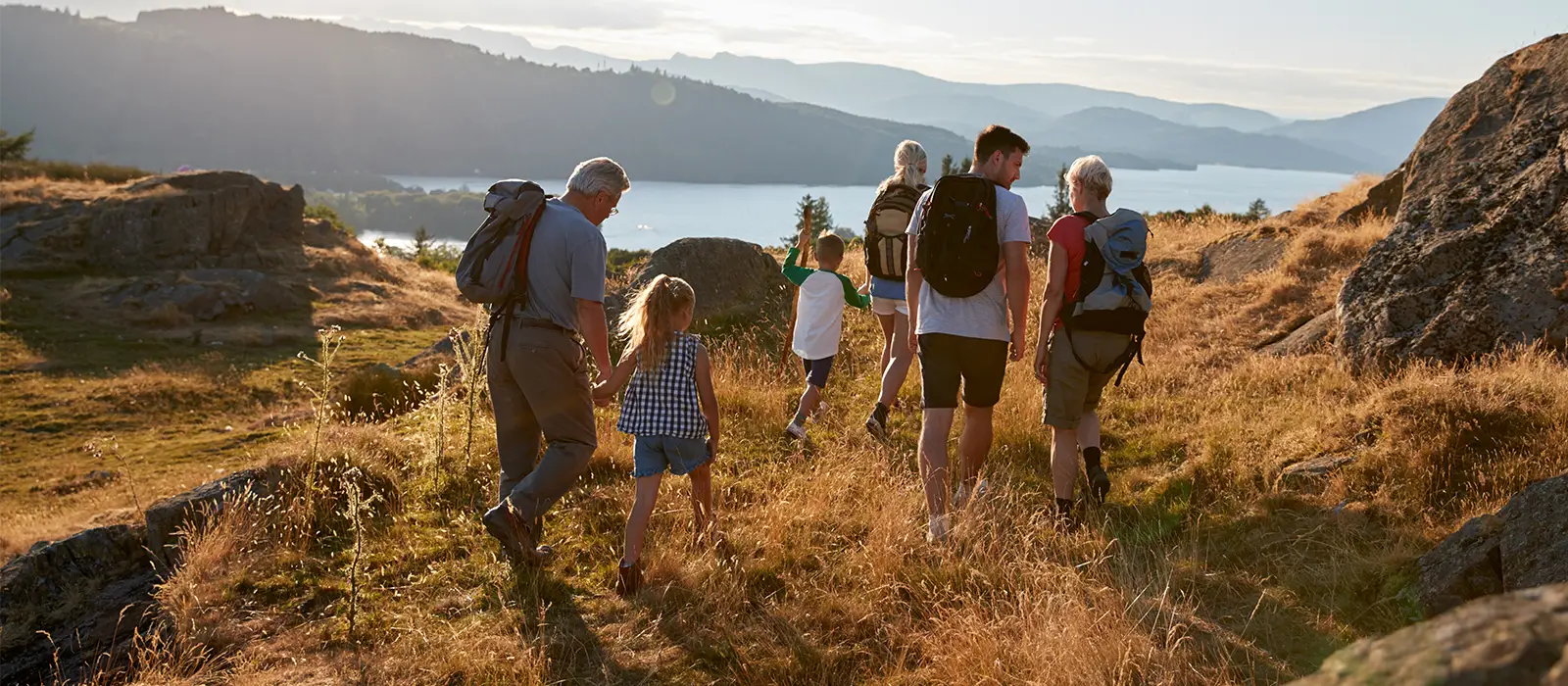 Rear View Of Multi Generation Family Walking On Top Of Hill On Hike Through Countryside.